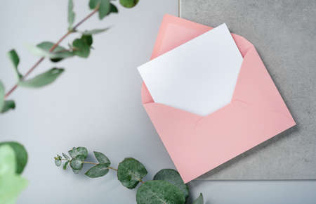 Real photo. Pink envelope square invitation card mockup with a eucalyptus branch. Top view with copy space, light gray background. Template for branding and advertisingの写真素材