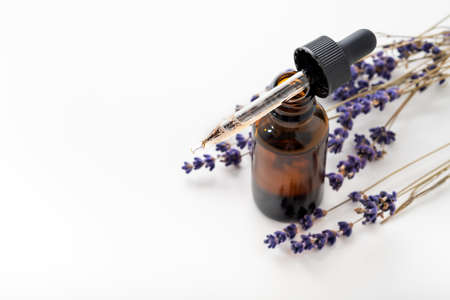 Essential oil with a dropper and lavender branches on a white background with copy space. Brown glass cosmetic bottle, serum.の写真素材