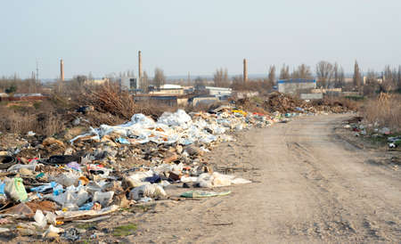 Illegal garbage dump on the road near the city, plastic and other waste. Dangerous pollution in nature. Terrible garbage on the background of industrial plantsの写真素材