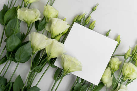 Real photo. square invitation card mockup with a eustoma flowers. Top view with copy space, light gray background. Template for branding and advertising.の写真素材