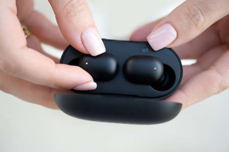 close-up of a woman taking out a black wireless earbud from his charging box. Female hands touching...