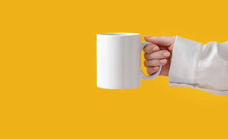 mockup ceramic white coffe cup or mug in female hands on yellow background with copy space. Blank template for your design, branding, business. Woman in shirt casual style. Real photo.の写真素材