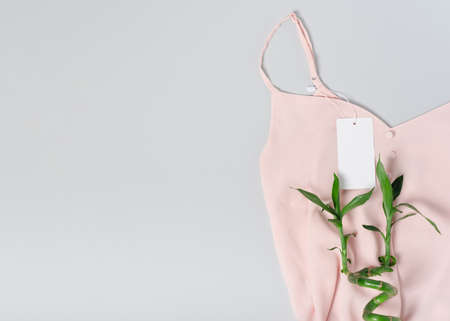White clothing tag, label blank mockup template, to place your design. On a premium cotton pink blouse fabric textile background. Bamboo. Flat lay copy spaceの写真素材