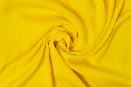 Soft bright yellow deluxe quality polyester fabric is rolled up in beautiful waves. Background.の写真素材