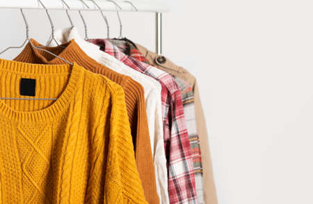 Autumn vintage clothing hangs on hangers on the rack. Beige trench coat, sweaters, plaid shirts. Organization of space, winter cleaning. Mockup, template.の写真素材