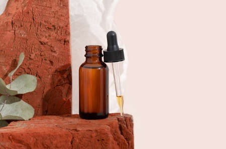 Mockup brown glass bottle with dropper serum on red stone and beige background with crumpled paper. Brutal. Copy space. Acid peeling, face oil, collagen.の写真素材