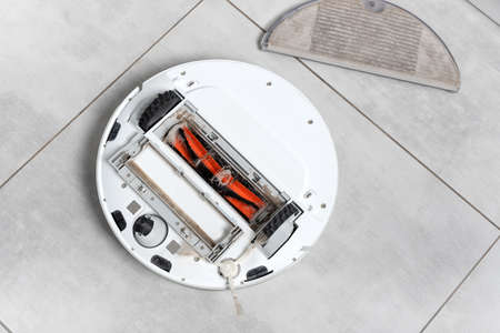 Washing robot vacuum cleaner white on the floor, dirty brush with female long hair and cat's pet hair. Cleaning the vacuum cleaner. dirty.の写真素材