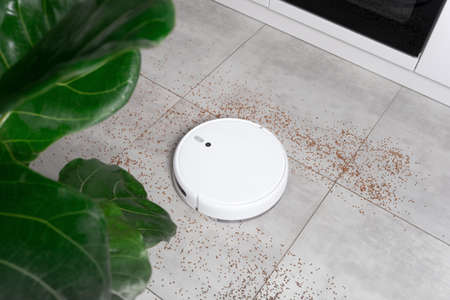 Washing White robot vacuum cleaner device cleaning floor from crumbs groats at home on utonite tiles in the kitchen.の写真素材
