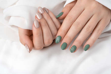 Hands of a young woman with green olive matte nails and beige glossy nails on a white background. Nails of different colors. Manicure, beauty salon. Copy space for text or logo. abstractの写真素材