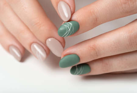 Hands of a young woman with green olive matte nails and beige glossy nails on a white background. Nails of different colors. Manicure, beauty salon. Copy space for text or logo. abstractの写真素材