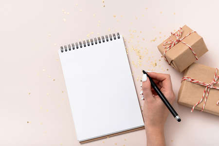 Female hand write hold notebook blank paper mockup, golden stars confetti, gift boxes on beige...