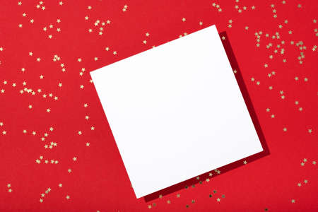 Christmas New year composition. Blank square paper mockup, golden stars confetti decore on red background. Flat lay, top view, copy space, minimalistの写真素材