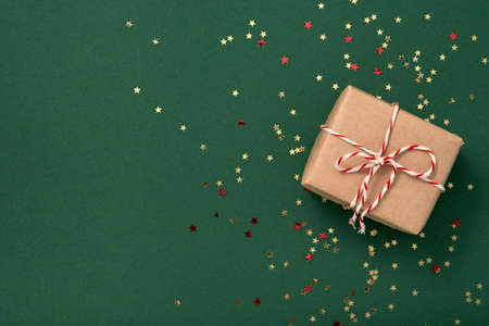 Gift boxe in craft paper with white-red New Year's ribbon and gold confetti stars on a green...