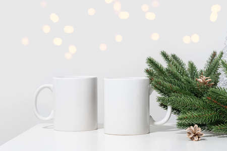 Christmas mockup two white empty tea mugs on a white table and branches of a Christmas tree wreath. Cup template for your design, logo with copy space. New Yearの写真素材