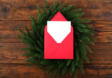 Blank square paper mockup envelope red on brown wooden vintage table background. Flat lay, top view, copy space, minimalist. Christmas and New Year concept. Fir wreathの写真素材