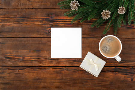 Blank square paper mockup gift box on brown wooden vintage table background. Flat lay, top view, copy space, minimalist. Christmas and New Year concept. Fir wreathの写真素材