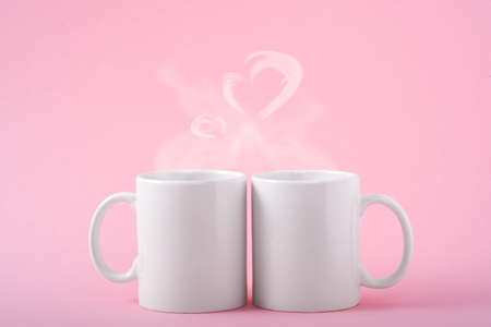 Mockup white coffe two cups or mug on a pink background with copy space. Blank template for your design, branding, business. real photo. Hot drink steam in the form of heartsの写真素材