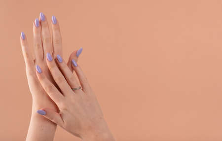 Hands of a beautiful well-groomed with feminine violet lavender nails gel polish on a beige background. Manicure, pedicure beauty salon concept.の写真素材