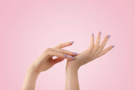 Hands of a beautiful well-groomed with feminine violet lavender nails gel polish on a pink background. Manicure, pedicure beauty salon concept.の写真素材