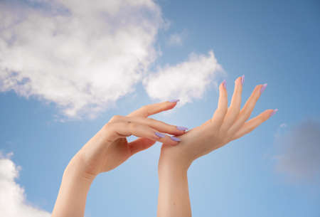 Hands of a beautiful well-groomed with feminine violet lavender nails gel polish on a sky blue background. Manicure, pedicure beauty salon concept.の写真素材