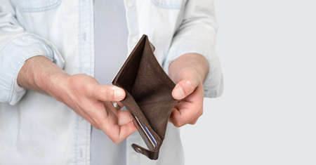 A man holds an empty brown purse with no money. Male hands. Bankruptcy, poverty. Isolated gray...