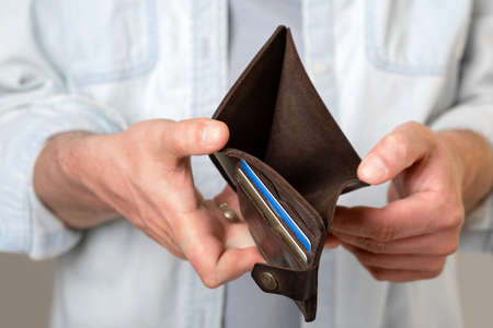 A man holds an empty brown purse with no money. Male hands. Bankruptcy, poverty. Isolated gray...