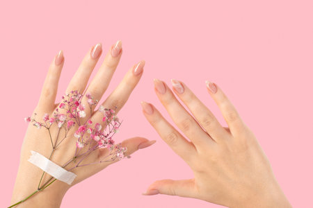 Female two hands with pink gypsophila flowers gel polish beige long nails on a pink isolated background. Beauty spa concept, manicure marble designの写真素材