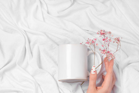 Women's hands hold a mockup of a white empty mug on a textile background, a cup for your design and close-up. White manicure nails with red hearts for Valentine's Day.の写真素材