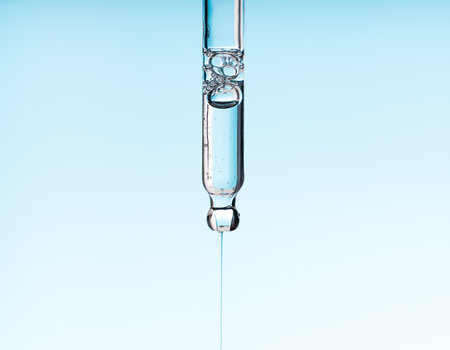 Pipette serum with clear liquid niacinamide, hyaluronic or Aha Bha acids on a blue white isolated background. Textured swatch skincare. Laboratory cosmeticの写真素材