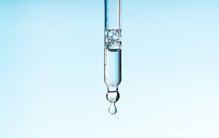 Pipette serum with clear liquid niacinamide, hyaluronic or Aha Bha acids on a blue white isolated background. Textured swatch skincare. Laboratory cosmeticの写真素材