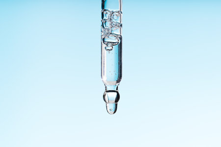 Pipette serum with clear liquid niacinamide, hyaluronic or Aha Bha acids on a blue white isolated background. Textured swatch skincare. Laboratory cosmeticの写真素材