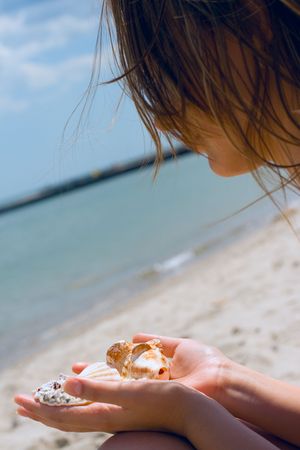 pretty girl at the beach with shells in her handsの写真素材