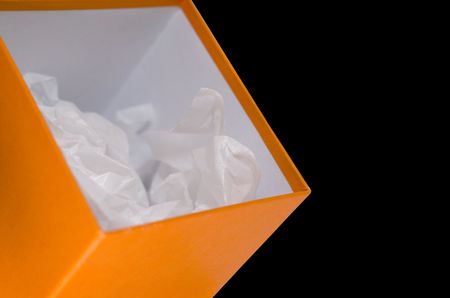 close up of orange opened box with white paper on black backgroundの写真素材