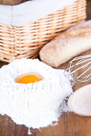 still life of bread, eggs, whisk and flour on a wooden board の写真素材