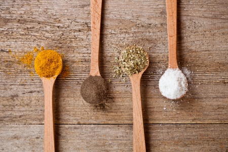 curry, pepper, oregano and cooking salt in wooden spoons on rustic wooden backgroundの写真素材