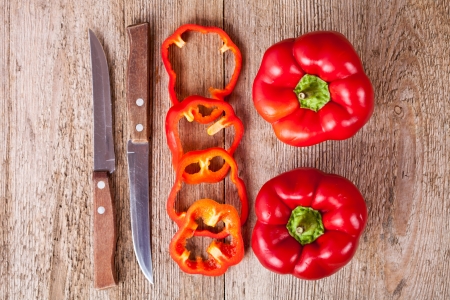 sliced and full red bell peppers and old knifes on rustic wooden tableの写真素材