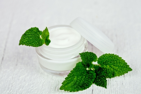 face cream in glass jar with green leaf of urtica on white wooden backgroundの写真素材