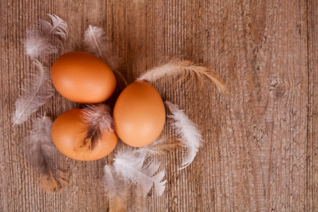 three eggs and feathers on rustic wooden tableの写真素材