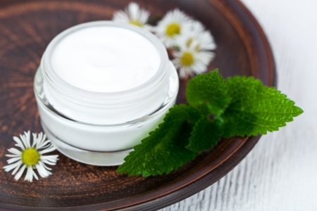 container with cream urtica and chamomiles on browm plateの写真素材