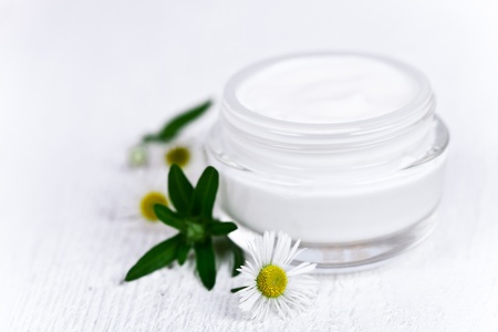 container with cream and chamomiles on white wooden  background