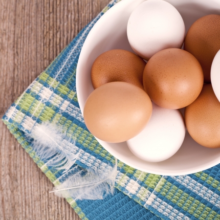 eggs in a bowl, towel and feathers on rustic wooden tableの写真素材