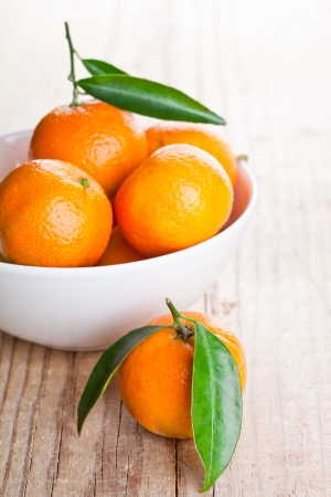 tangerines with leaves in bowl on wooden tableの写真素材