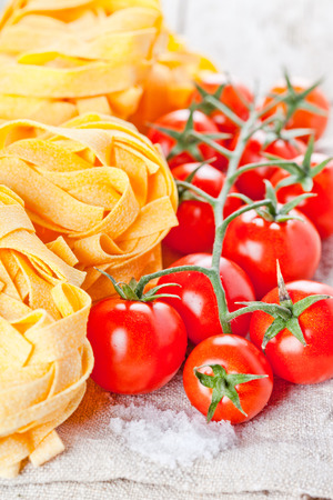 uncooked pasta and fresh tomatoes on texlile background の写真素材