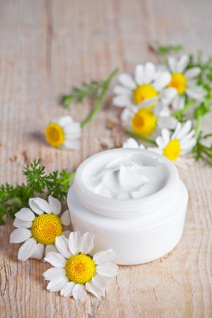 container with cream and chamomiles on wooden background の写真素材
