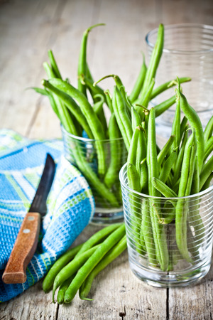 green string beans in glasses, napkin and knife closeup on rustic wooden backgroundの写真素材