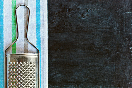 metal grater and tablecloth over blackboard background