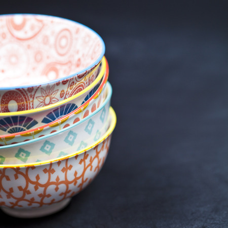 Stack of colorful empty ceramic bowls closeup on black board background. With copy space.の写真素材
