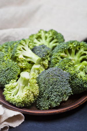 Fresh green organic broccoli in brown plate and linen napkin closeup on black board background.の写真素材