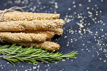 Italian grissini bread sticks with sesame and rosemary herb on black board background closeup image....