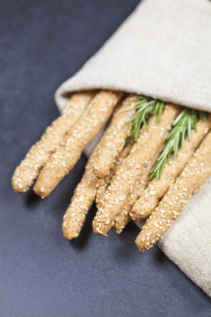 Italian grissini bread sticks with sesame and rosemary herb on black board background. Fresh italian snack.の写真素材